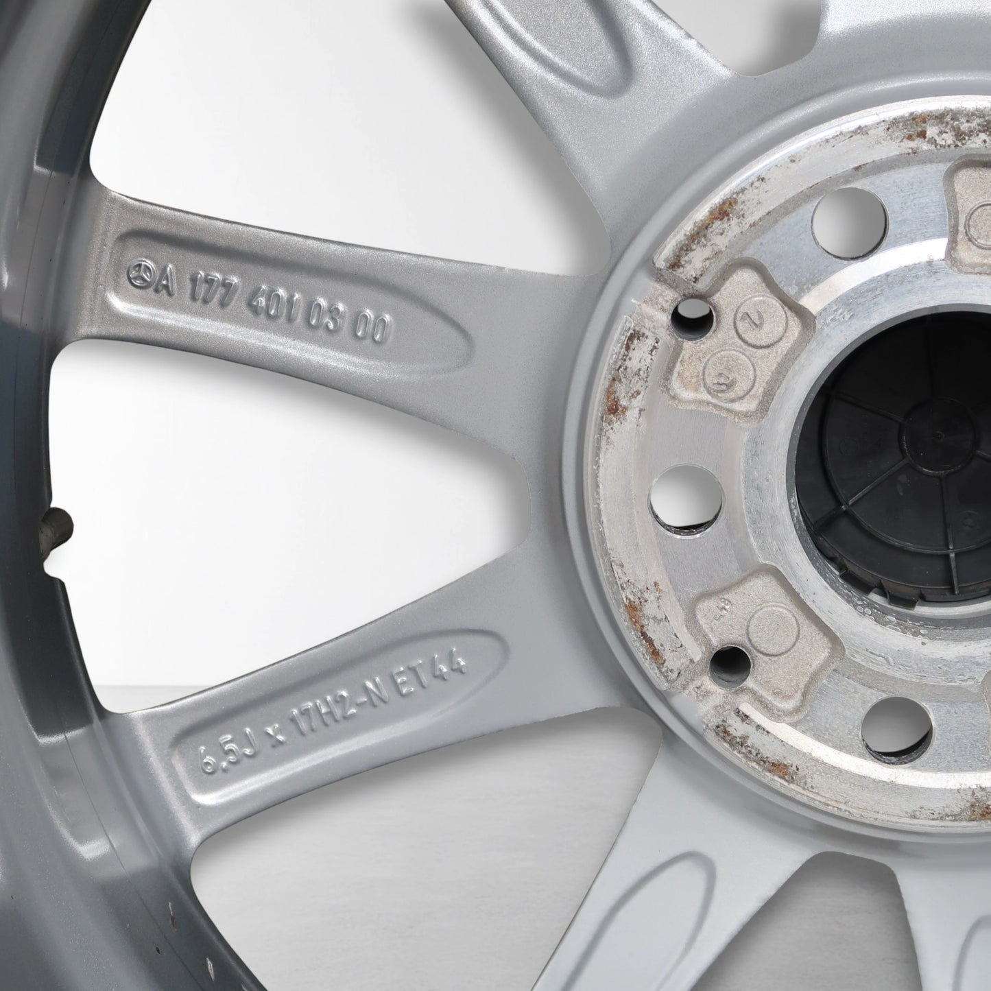Close-up van zilverkleurige velg met gegraveerde codes en lichte roest rond naafdop