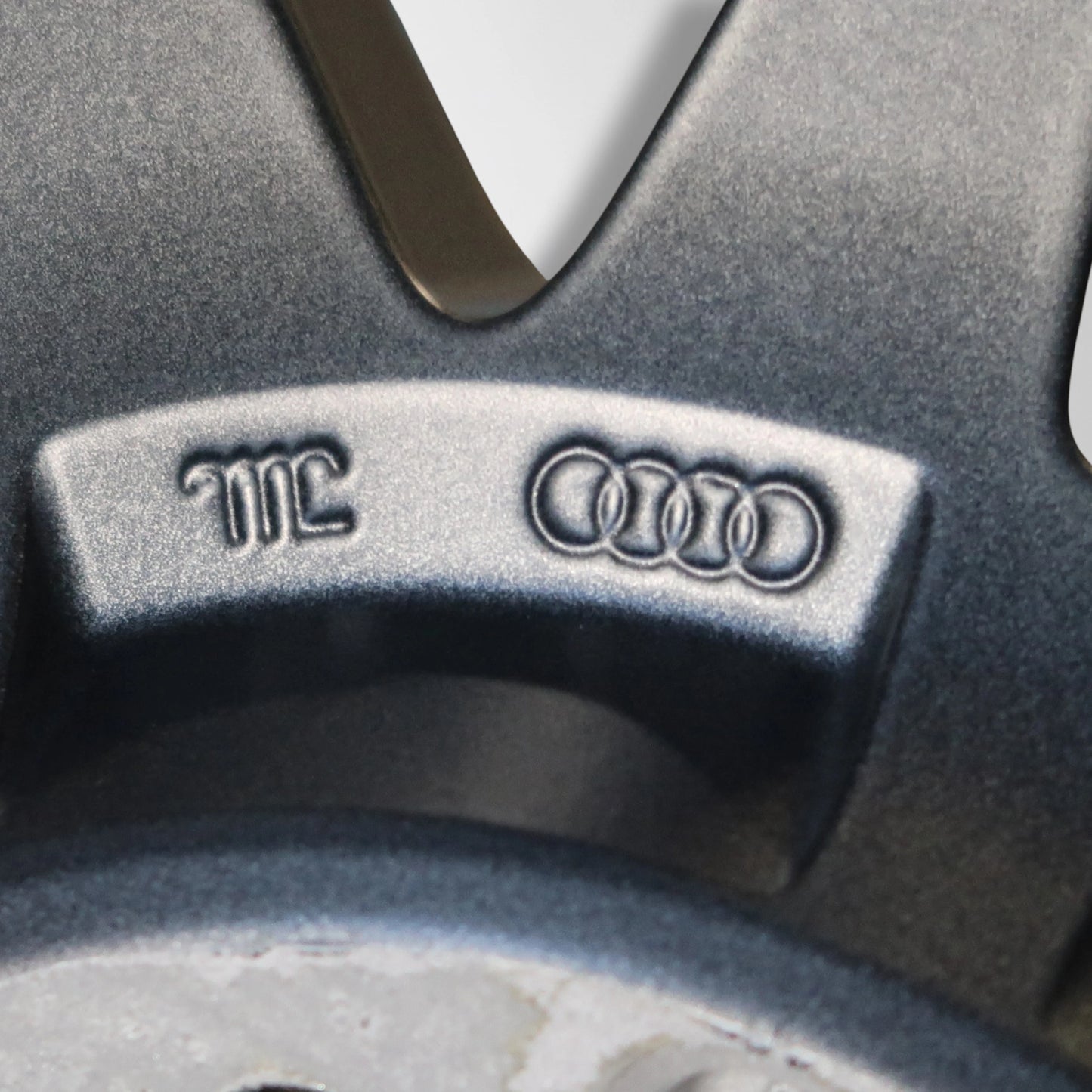 Close-up van Audi- embleem en markering op donkergrijze velg, met reliëfletters.