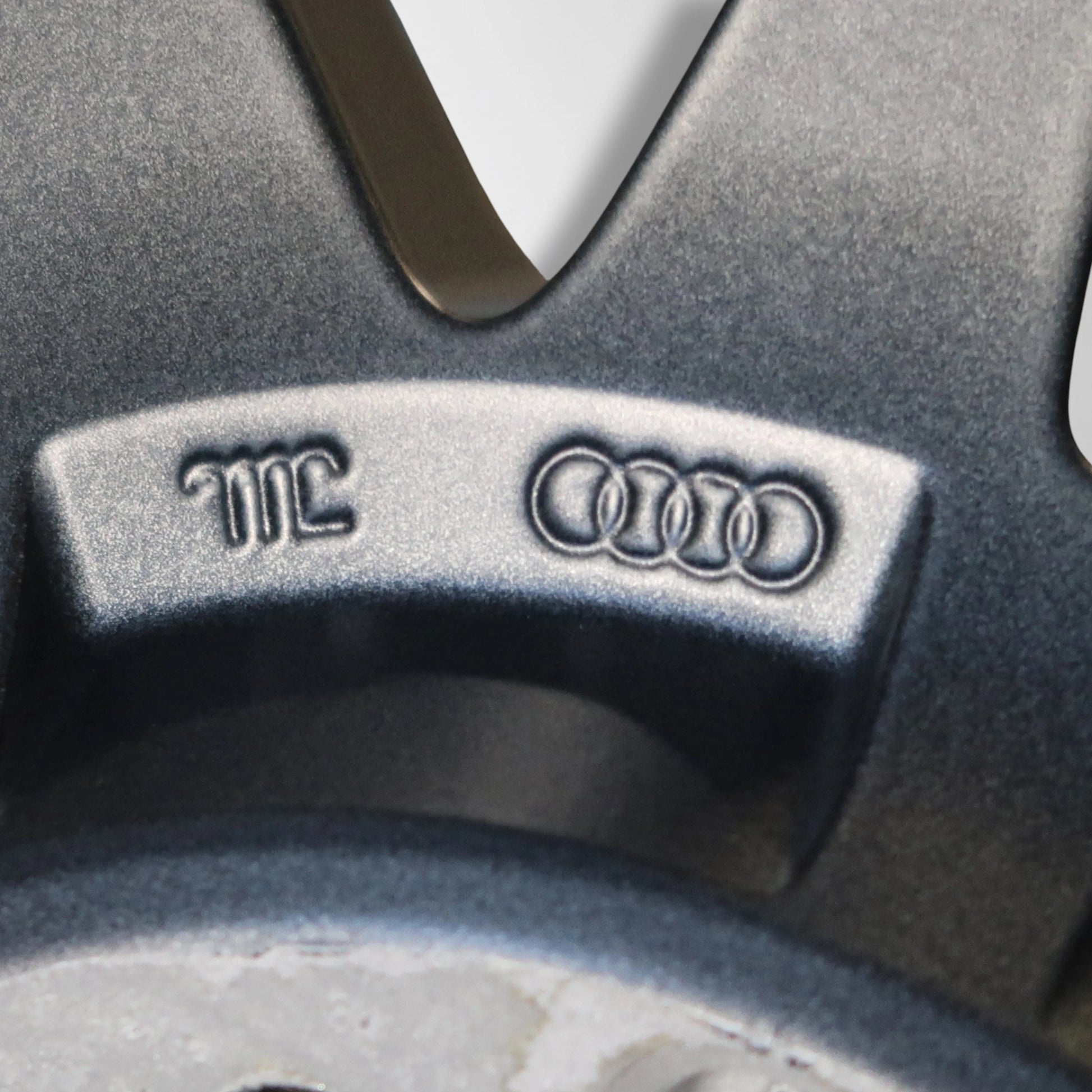 Close-up van Audi- embleem en markering op donkergrijze velg, met reliëfletters.