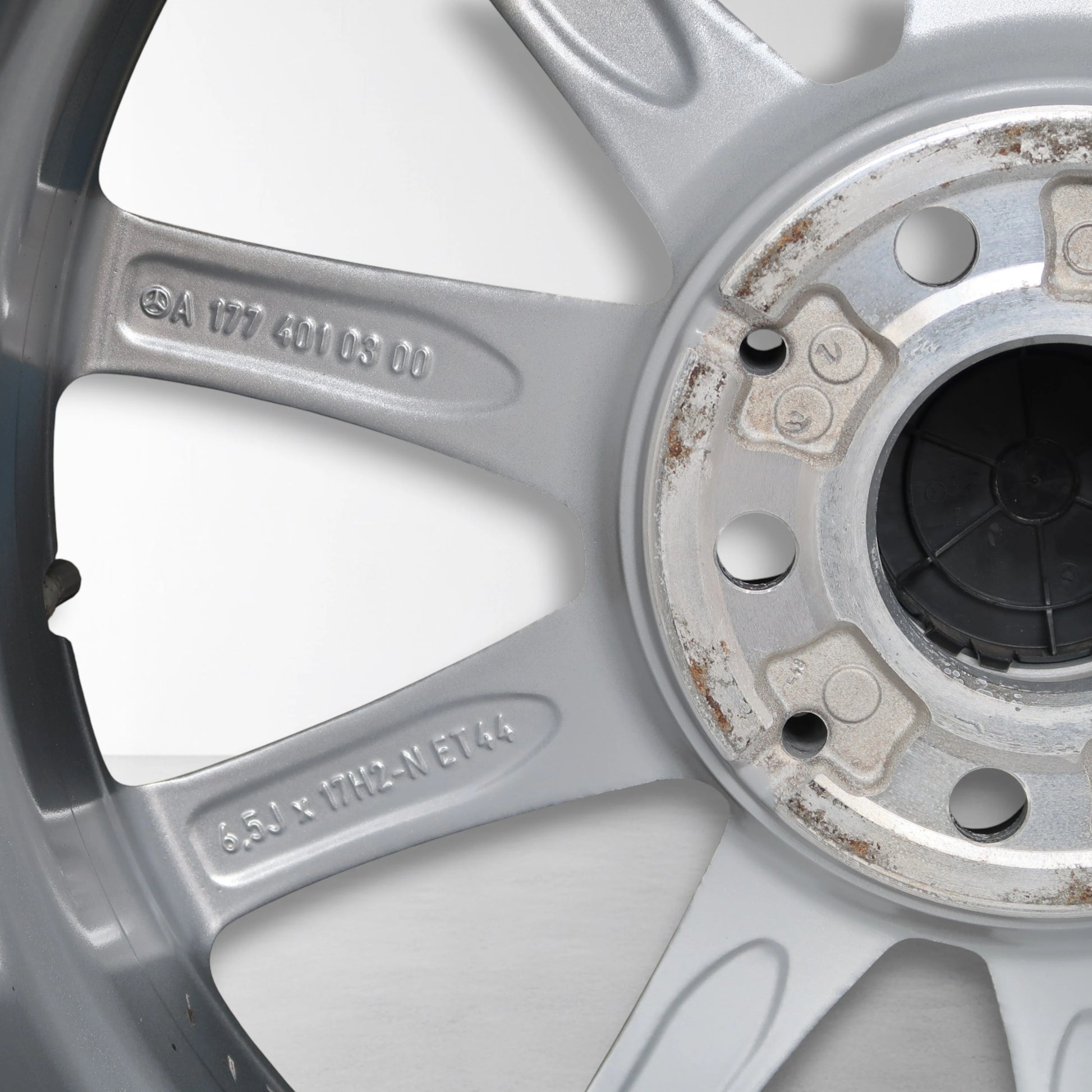 Close-up van zilverkleurige velg met gegraveerde codes en lichte roest rond naafdop