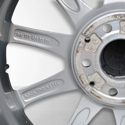 Close-up van zilverkleurige velg met gegraveerde codes en lichte roest rond naafdop